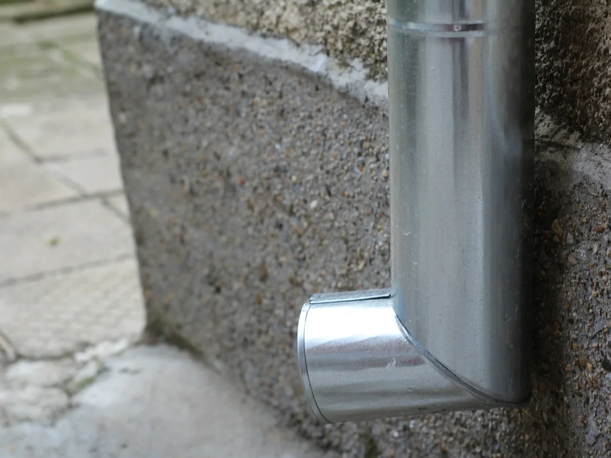 Metal rainwater downpipe detail Close-up of a metal rainwater downpipe and its lower bend beside a wall