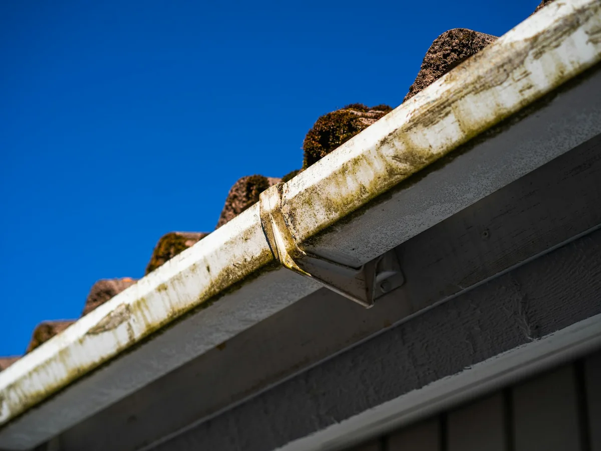 Weathered guttering and roof tiles photographed against a blue sky