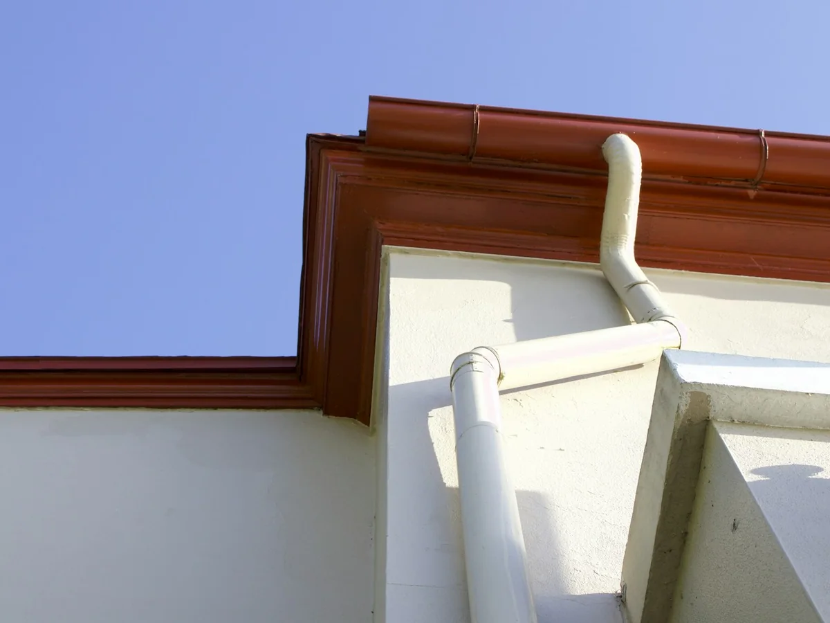 Gutter and downpipe connection White downpipe connected to guttering beneath a roof edge